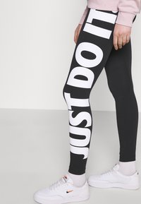 Svarta leggings med stor vit "JUST DO IT"-tryck på sidan, tillverkade av stretchigt material. Kombinerade med vita sneakers.