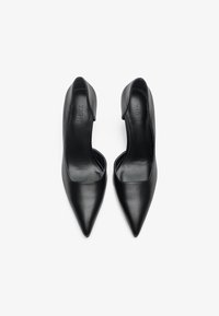 Tacones de cuero negro con puntera afilada y diseño de parte trasera abierta. Textura suave, estilo minimalista y una silueta elegante.