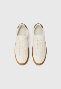 White leather sneakers with a textured gum sole, featuring a rounded toe, lace-up design, and a dark green accent on the heel.