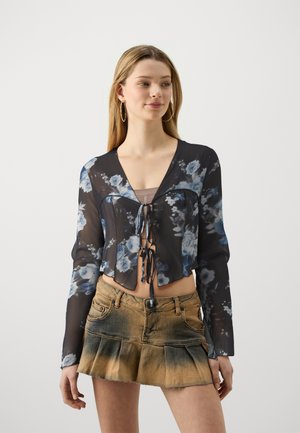 Black sheer blouse with floral blue patterns, V-neckline, and tie closure at front. Paired with a faded denim pleated skirt.
