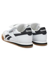 Baltas ādas kedas ar melniem akcentiem un Reebok zīmolu, ar mīkstu apkakli un mēli, gumijas zoli un aizdari ar āķi un cilpu.