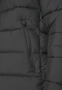 Tissu de veste matelassée noire avec un gros plan sur une poche zippée verticale noire et des détails de couture visibles.