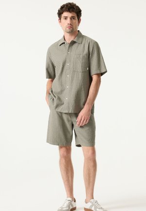 Groen gestructureerd shirt met korte mouwen en bijpassende korte broek, voorzien van een zak, knopen en een losse pasvorm, gecombineerd met lichte sneakers.