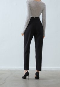 Pantalon noir taille haute avec une coupe ajustée et des jambes fuselées. Associé à un haut gris à manches longues et des talons hauts noirs.