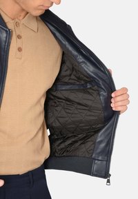 Giubbotto di pelle blu navy con fodera nera trapuntata. Chiusura a zip e dettagli a costine sull'orlo. Aperto per mostrare le caratteristiche e la texture interne.