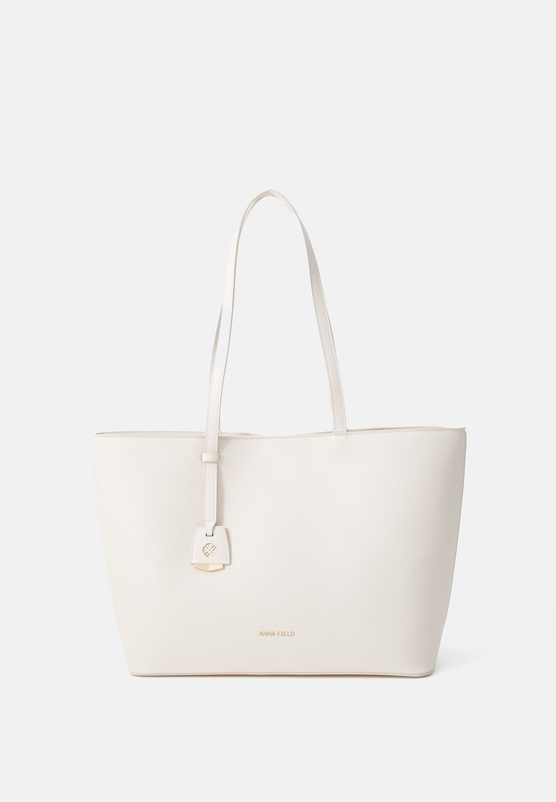 Light beige tote bag made of textured material, featuring two long handles and a decorative padlock accent on the front.