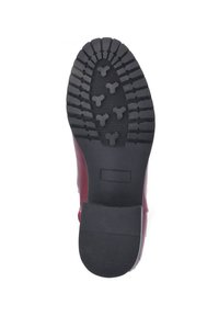 Sole di una scarpa bordeaux, con profili profondi e schemi triangolari, superficie nera in gomma testurizzata e sezione del tacco liscia.