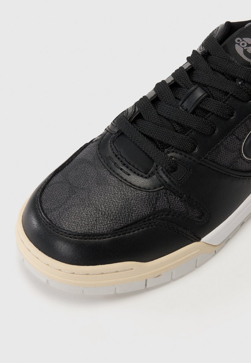 Zwarte sneaker met een gestructureerde leren bovenkant, contrasterende gladde rubberen zool en zwarte veters. Inclusief een subtiel logo aan de zijkant.