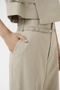 Beige, teksturert todelt antrekk med en cropped topp og høytlivsbukser med belte og metalløyer; lomme på siden.