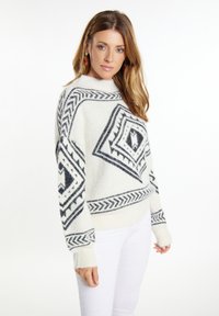 Maglione bianco a maglia con motivo geometrico nero, dotato di un collo alto e maniche lunghe. Tessuto morbido con polsini e orlo a coste.