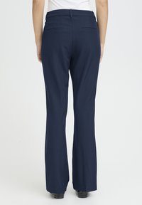 Pantalon bleu marine sur mesure avec une coupe évasée, doté de deux poches arrière et d'une texture de tissu lisse et légère.