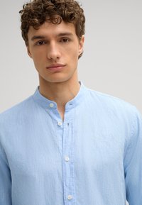 Camicia azzurro chiaro con colletto, realizzata in tessuto texture, dotata di una chiusura con bottoni bianchi e una vestibilità comoda. Nessun motivo visibile.