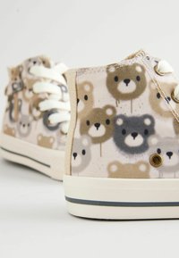 Zapatillas altas de lona con un patrón de cara de oso en tonos beige y marrón, con cordones blancos y una suela de goma acentuada por una franja oscura.