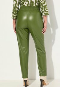 Zielone spodnie z ekologicznej skóry o gładkiej fakturze, dopasowanym kroju i elastycznym pasie, zestawione z kremowymi butami na wysokim obcasie.