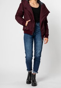 Burgundy huva-jacka med dragkedja fram, ribbade ärmslut och sidofickor, i kombination med blå jeans med uppvikta ben och svarta ankelstövlar.