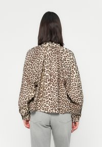 Blusa a stampa leopardata in beige e marrone, a maniche lunghe, con una parte posteriore plissettata, abbinata a jeans grigi, che enfatizzano la texture del tessuto.