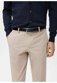 Cardigan azul marino abotonado combinado con pantalones beige. Los pantalones tienen una textura suave y bolsillos frontales, asegurados con un cinturón negro y hebilla plateada.