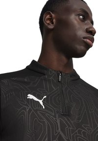 Schwarzes sportliches Zip-up-Oberteil mit geometrischem Muster, hoher Kragen und weißem Puma-Logo. Die glatte Textur und das figurnahe Design verbessern die Funktionalität.