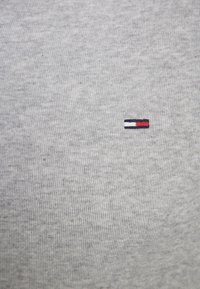 Szary bawełniany T-shirt o fakturowanej powierzchni. Z przodu znajduje się małe haftowane logo w kolorach czerwonym, białym i granatowym.