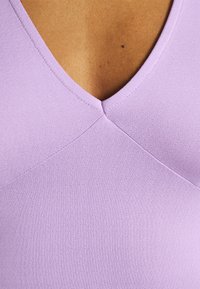 Lila v-ringad topp med en figursydd design. Har en mjuk, ribbad textur och diagonala sömsdetaljer.