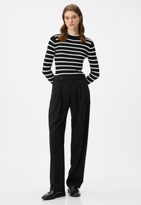 Nauha musta-valkoinen ribattu neule yhdistettynä korkeavyötäröisiin mustiin housuihin, joissa on etupleatit ja yksi nappi. Kiiltävät mustat kengät.