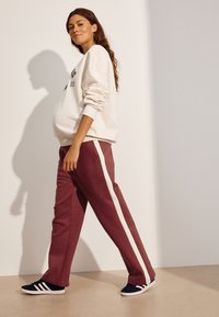 Cremefarvet sweatshirt med sort grafisk tekst, kombineret med bordeaux sweatpants med hvide sidestriber. Sorte træningssko med hvide detaljer.