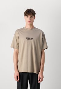 Beež puuvillane T-särk lühikeste varrukatega, ümar kaelus ja must trükitud "BARBOUR INTERNATIONAL" logo rinnal.