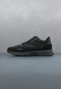 Baskets basses noires à lacets avec semelle texturée et marquage "BOSS" sur le côté et le talon, posées sur un fond gris.