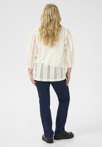 White lace knit top with puff sleeves and a straight hem, paired with dark blue jeans and black platform shoes. Back view.