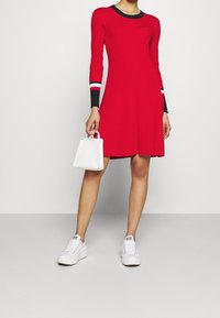 Punainen ribattudressi, jossa on pitkät hihat, tummansiniset yksityiskohdat ja valkoiset raidat hihojen suissa. Yhdistetty valkoisiin tennareihin ja pieniin valkoisiin laukkuun.