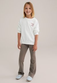 Biała bluza z napisem "YOUNG AND FREE" w czerwonym kolorze, zestawiona z jasnoszarymi spodniami w paski o rozszerzanej nogawce oraz niebieskimi butami sportowymi. Gładki, casualowy wygląd.