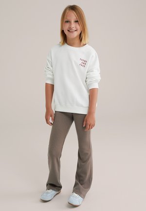 Felpa bianca con scritta rossa "YOUNG AND FREE", abbinata a pantaloni svasati a righe grigie chiare e scarpe da ginnastica blu. Look semplice e casual.