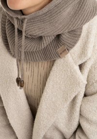 Taupe col met een rib gebreid ontwerp. Voorzien van verstelbare koordjes met houten kralen en een klein merklabel.