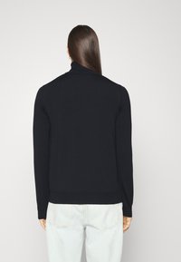 Czarny, prążkowany sweter z golfem, z długimi rękawami, dopasowany w talii, na neutralnym tle. Gładka, miękka faktura.