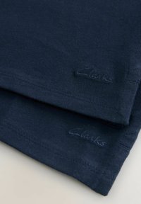 Marinblå bomullstyg med en mjuk textur, prydd med sömmar och en broderad "Clarks"-logotyp i matchande marinblå färg vid nederkanten.