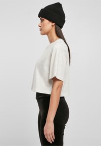Camiseta corta de color gris claro con mangas cortas, combinada con leggins negros de cintura alta. El modelo lleva un gorro de lana negro.