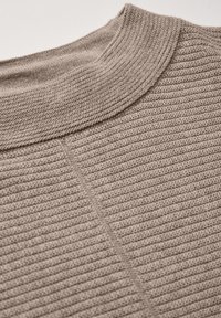 Beige ribbad stickad tröja med rund halsringning, med ett strukturerat mönster och en slät finish vid kragen.