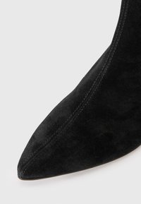 Bottine en suede noir avec un bout pointu, une texture lisse et un minimum de coutures sur les côtés.