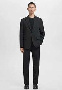 Un costume noir avec un blazer structuré, un devant à un bouton et deux poches avant, associé à un pantalon assorti et des chaussures noires.