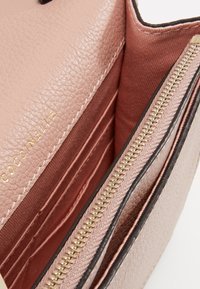 Interiören av en rosa läderväska med ett fack med dragkedja och flera kortfack. Slät textur med detaljer i guld.