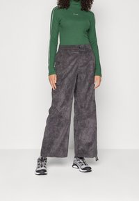 Grå vide byxor i mjukt, texturerat material med sidofickor. Kombineras med en grön polotröja med vita ränder och en logotyp.