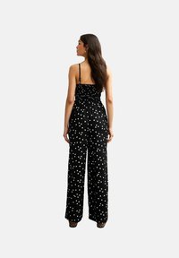 Completo nero con pois bianchi, corpino aderente, pantaloni larghi, spalline sottili e schiena arricciata. Tessuto morbido e vestibilità comoda.
