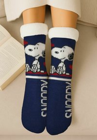 Navy blue socks featuring a white and black Snoopy design with red accents. Soft, fuzzy white cuffs. Knit texture with text "Snoopy" on the foot.