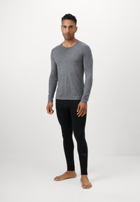 Chemise à manches longues grise en tissu doux, associée à des leggings noirs ajustés. Les leggings comportent un petit logo près de la cheville.