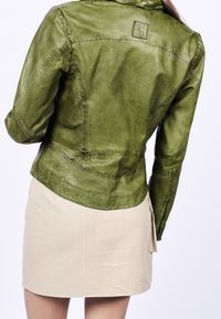 Grüne Lederjacke mit tailliertem Schnitt, sichtbaren Nähten und einem dezenten Logodetail auf der Rückseite. Kombiniert mit einem hellbeigen Rock.