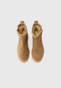 Bruine suède enkellaarsjes met een zachte, donzige beige voering en een lussenaccent aan de achterkant. Platte rubberen zolen en minimale stikdetails.