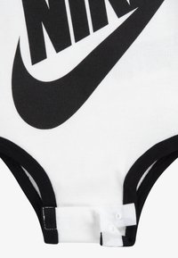 Juodai balta bodysuit, pagaminta iš medvilnės, su dideliu juodu Nike logotipu, juoda apykakle ir mygtukais apačioje.