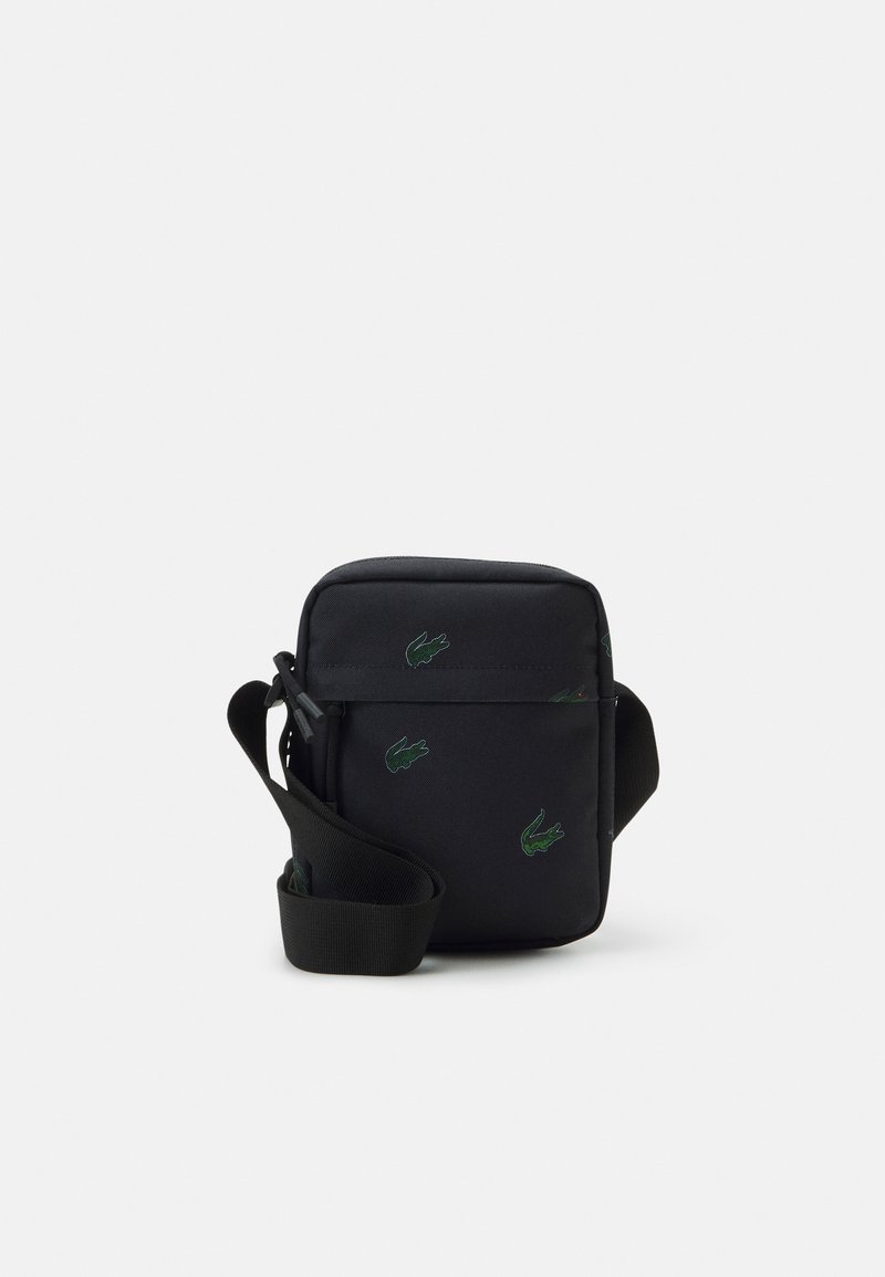 Sac bandoulière noir avec une sangle réglable, orné de plusieurs petits logos crocodile verts à l'avant et sur les côtés.