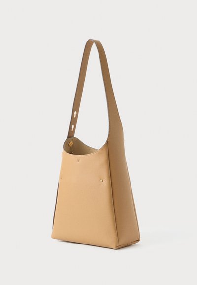 Sac à épaule en cuir tan avec une texture lisse, un design minimaliste et une large ouverture. Présente des coutures visibles et de subtils accents dorés.