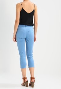 Blue capri pants made of soft fabric, featuring a fitted design and two back pockets. Paired with a black spaghetti strap top and brown heels.